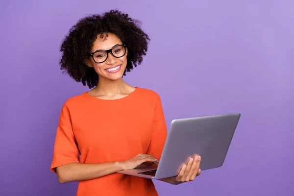 Foto de la señora divertida millennial tipo portátil usar camiseta naranja aislada sobre fondo de color violeta — Foto de Stock