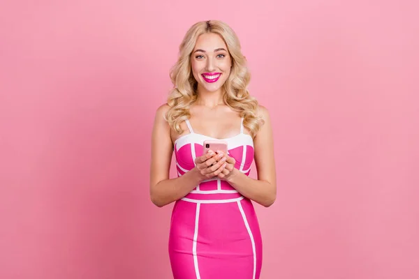 Retrato de atractiva chica alegre femenina de pelo ondulado utilizando dispositivo de chat aislado sobre fondo de color pastel rosa —  Fotos de Stock