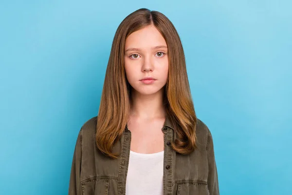Портрет молодой, довольно серьезной девушки в зеленой рубашке с длинными каштановыми волосами на голубом фоне — стоковое фото