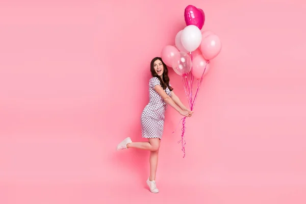 Foto de divertida señora funky vestido con puntos vestido sosteniendo globos caminando aislado color rosa fondo — Foto de Stock