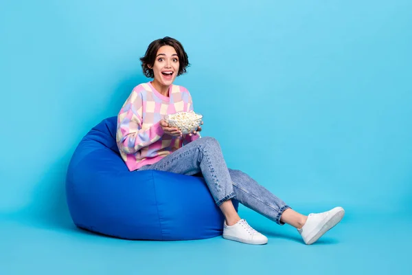 Full Size Profilseite Foto von jungen Mädchen sitzen Sitzsack essen Popcorn Uhrenfilm isoliert über blauem Farbhintergrund — Stockfoto