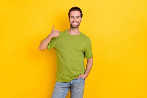 Havalı sakallı genç adamın fotoğrafı baş parmağını gösteriyor. Sarı arka planda izole edilmiş tişört kotu giyiyor. — Stok fotoğraf