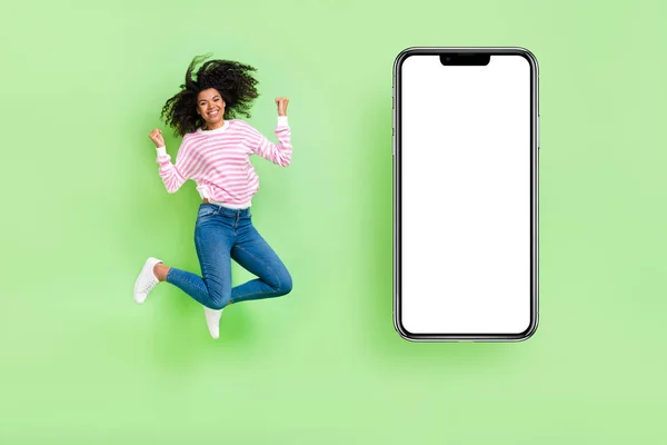 Pleine longueur vue de joyeuse fille chanceuse saut se réjouir gagner téléphone portable annonces affiche isolé fond de couleur vert vif — Photo