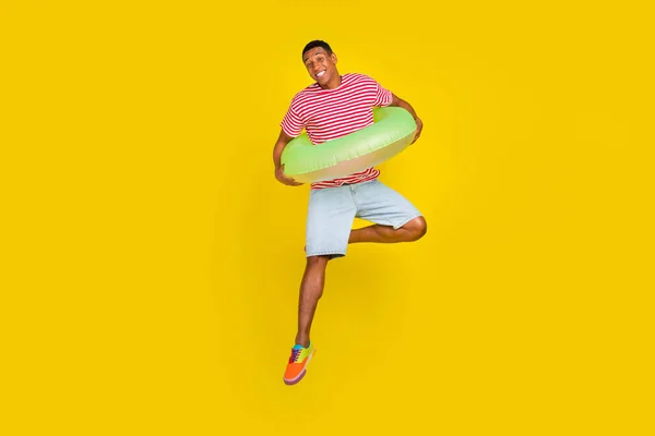 Plná velikost fotografie chlapa držet plavec prsten skok nosit červené pruhované oblečení izolované přes žlutou barvu pozadí — Stock fotografie