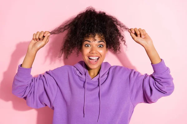 Fotografie dojem lesklé afro dívka nosit fialovou mikinu držení rukou ruce vlasy kadeře s úsměvem izolované růžové barvy pozadí — Stock fotografie