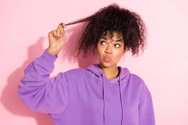 Photo of dreamy doubtful lady dressed purple hoodie lips pouted hand arm hair curl looking empty space isolated pink color background