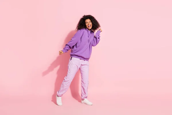 Parlak, şanslı afro kızın fotoğrafı menekşe rengi sweatshirt giyip boş alanda dans ediyor yumruğunu kaldırarak gülümsüyor pembe arka plan — Stok fotoğraf