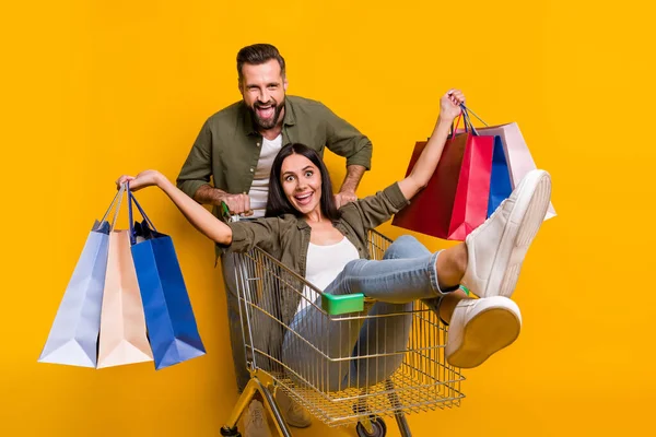 Foto de pareja alegre joven tienen tienda de diversión descuento vacaciones regalo carro tienda aislado sobre fondo de color amarillo — Foto de Stock