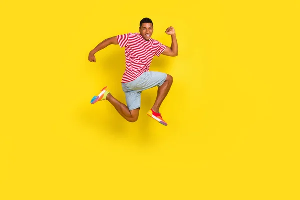 Full kropp profil sida foto av killen hoppa springa snabbt copyspace slitage randiga kläder färg skor isolerad över glans gul bakgrund — Stockfoto