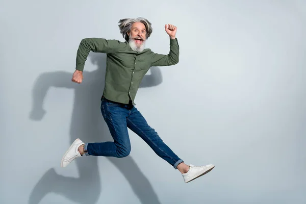 Foto av upphetsad pensionerad man bära grön skjorta hoppa högt kör snabbt tomt utrymme isolerad grå färg bakgrund — Stockfoto