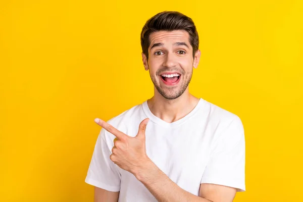 Foto van indrukwekkende jonge brunet guy index lege ruimte dragen witte t-shirt geïsoleerd op gele kleur achtergrond — Stockfoto