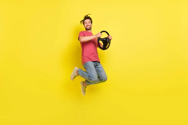フルサイズプロフィール写真のクールなひげ若い男のドライブ車は赤いTシャツのジーンズの靴を着用黄色の背景に隔離 — ストック写真