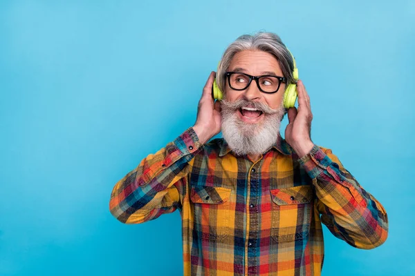 Hayalperest emeklinin kareli gömlek gözlükleriyle müzik dinlerken çekilmiş bir fotoğrafı. Boş alan, izole edilmiş mavi arka plan. — Stok fotoğraf