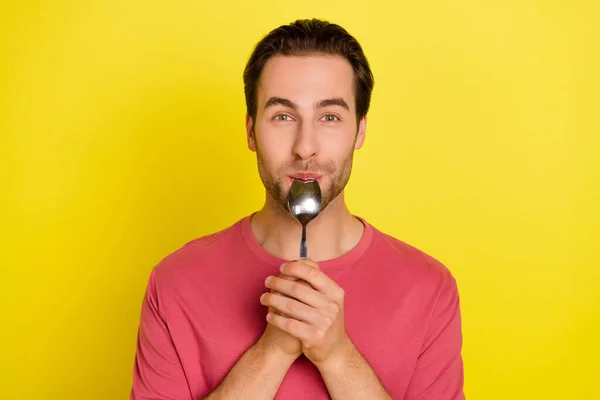 Фото позитивного смешного парня лизать ложку насладиться вкусной едой носить розовую футболку изолированный желтый цвет фона — стоковое фото