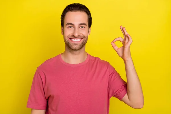 Bild av glad glad kille visa okey symbol strålande leende bära rosa t-shirt isolerad gul färg bakgrund — Stockfoto