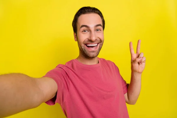 Zdjęcie przyjazny szalony podekscytowany facet pokazać v-sign wziąć autoportret nosić różowy t-shirt odizolowany żółty kolor tła — Zdjęcie stockowe