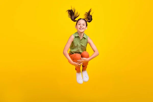 Foto de menina estudante despreocupado doce usar camisa verde sorrindo saltando alto isolado fundo de cor amarela — Fotografia de Stock