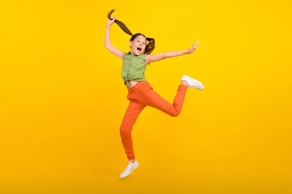 Foto de adorável menina estudante brilhante usar camisa verde sorrindo saltando alto correndo rápido isolado cor amarela fundo — Fotografia de Stock