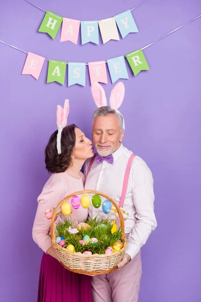 Verticale foto van twee oude vreedzame partners kus wang houden eieren voedsel mand geïsoleerd op violette kleur achtergrond — Stockfoto