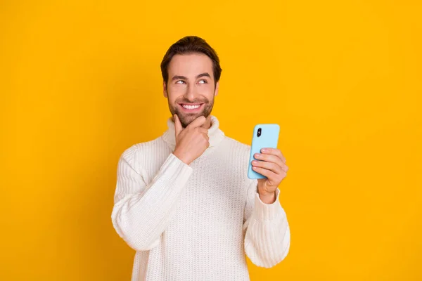 Foto van intelligente man houden telefoon vinger kin look lege ruimte dragen witte trui geïsoleerde gele kleur achtergrond — Stockfoto