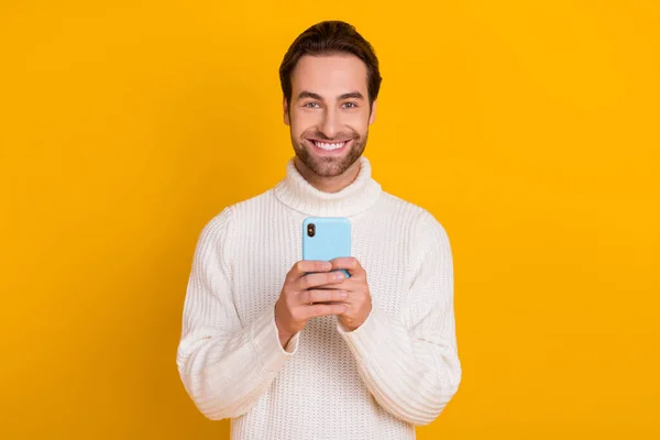 Foto van vrolijke populaire man houden telefoon genieten van positieve feedback dragen witte trui geïsoleerde gele kleur achtergrond — Stockfoto
