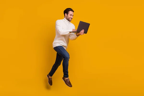 Photo of positive pretty guy wear white pullover jumping high writing modern device isolated yellow color background