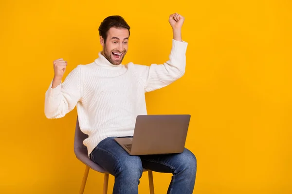 Foto de tipo afortunado vestido suéter blanco sentado silla de oficina lectura gadget levantamiento puños aislado color amarillo fondo — Foto de Stock