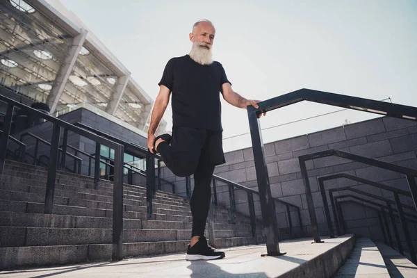 Full size φωτογραφία του ηλικιωμένου λευκό μαλλιά ταιριάζει άνθρωπος να τεντώσει φορούν μαύρο t-shirt σορτς sneakers έξω στην πόλη — Φωτογραφία Αρχείου