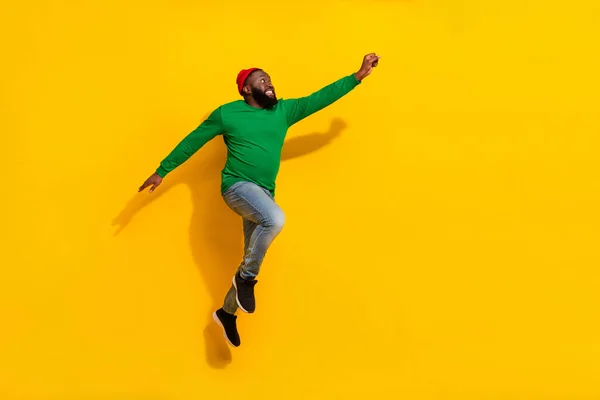 Profil foto av energisk hjälte kille hoppa njuta av flygning bära röd mössa grön skjorta isolerad gul färg bakgrund — Stockfoto