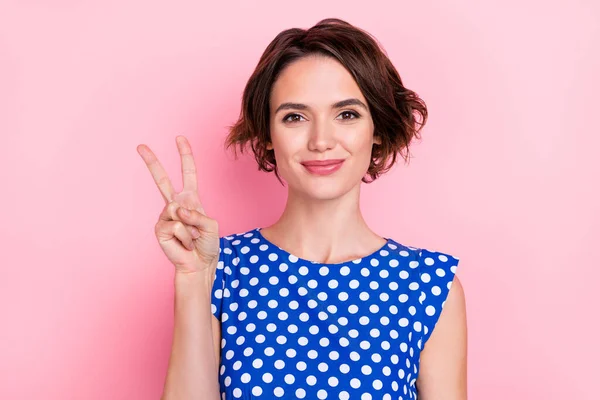 Foto de jovem muito feminino feminino em azul pontilhado vestuário mostrando v-sinal isolado no fundo cor-de-rosa — Fotografia de Stock