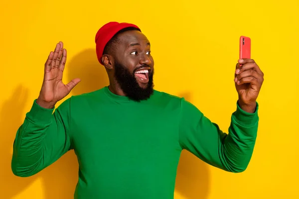 Fotografie radostného blogger muž držet telefon vlna ruka nosit červené beanie zelená košile izolované žluté barvy pozadí — Stock fotografie