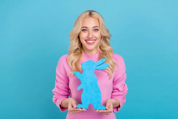 Retrato de atractiva chica de pelo ondulado alegre sosteniendo en las manos figura de liebre aislada sobre fondo de color azul brillante —  Fotos de Stock