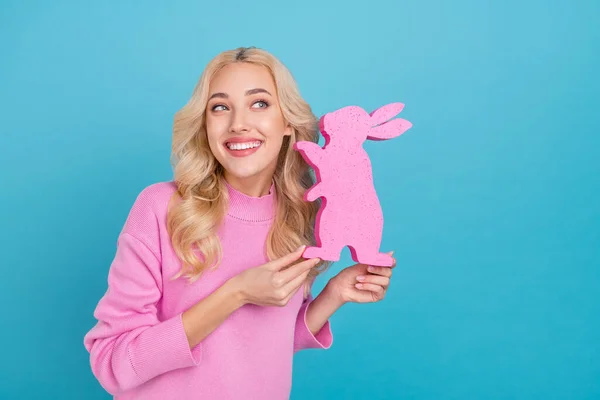 Foto von funky millennial lockige blonde Dame halten Hase tragen rosa Pullover isoliert auf blauem Hintergrund — Stockfoto