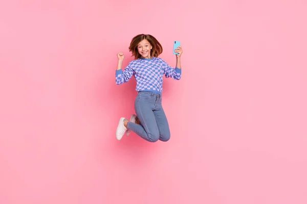 Plné tělo fotografie blond dospívající dívka skok držet telefon nosit svetr džíny boty izolované na růžovém pozadí — Stock fotografie