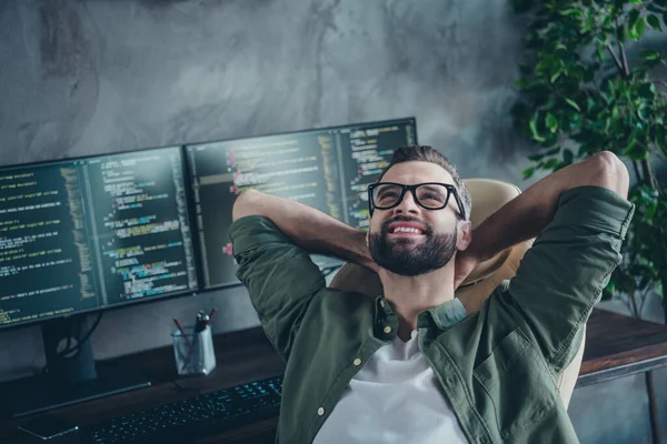 Фото умного мечтательного мужчины в зеленых очках рубашки, отдыхающего после разработки программного обеспечения руки за головой мастерской рабочее место — стоковое фото