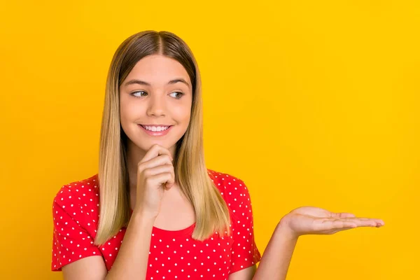 Porträtt av positiva sinnade flicka hand på haka titta intresserad handflata hålla tomt utrymme isolerad på gul färg bakgrund — Stockfoto