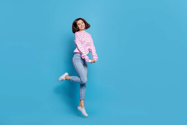 可爱的千禧年女士跳跃时穿着蓝色背景的衬衫牛仔裤鞋的全貌照片 — 图库照片
