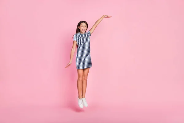 Foto de menina bonita doce vestido vestido listrado mostrando braço espaço vazio saltando isolado cor rosa fundo — Fotografia de Stock