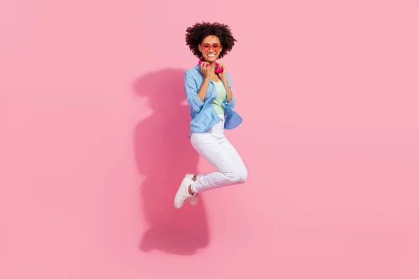 Foto de linda encantadora dama hipster salto han usado auriculares vaqueros camisa pantalones zapatillas aisladas de color rosa fondo —  Fotos de Stock