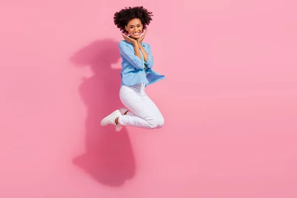 Foto de niña adorable inspirada bonita dama salto manos mejillas usar vaqueros camisa pantalones zapatillas aislado color rosa fondo — Foto de Stock
