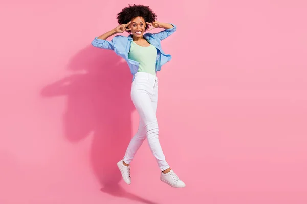 Foto de bonito funky bonita señora salto espectáculo v-signo de correr desgaste vaquero camisa pantalones zapatillas aisladas de color rosa fondo —  Fotos de Stock