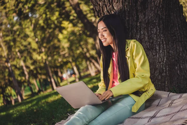Портрет привлекательной дружелюбной веселой мечтательной девушки, сидящей на обложке с помощью ноутбука, печатая электронную почту отдыха времяпрепровождение свежий воздух на открытом воздухе — стоковое фото