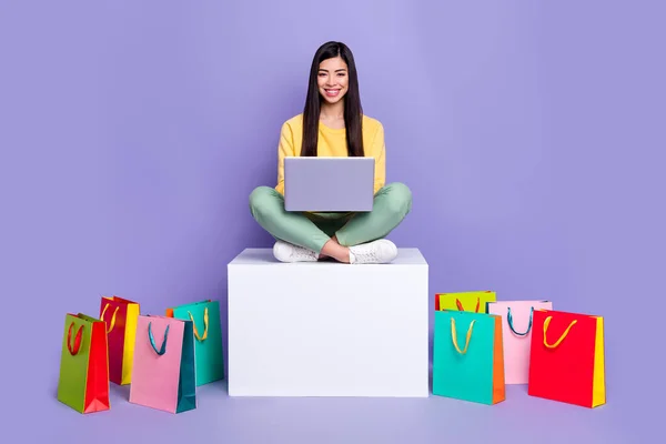 Foto de tamaño completo de niña sentarse podio uso portátil tienda boutique nueva colección aislada sobre fondo de color violeta —  Fotos de Stock