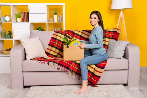 Foto de perfil de tamaño completo de la señora positiva sentada sofá caja de cartón cosas aisladas en el fondo de color amarillo —  Fotos de Stock