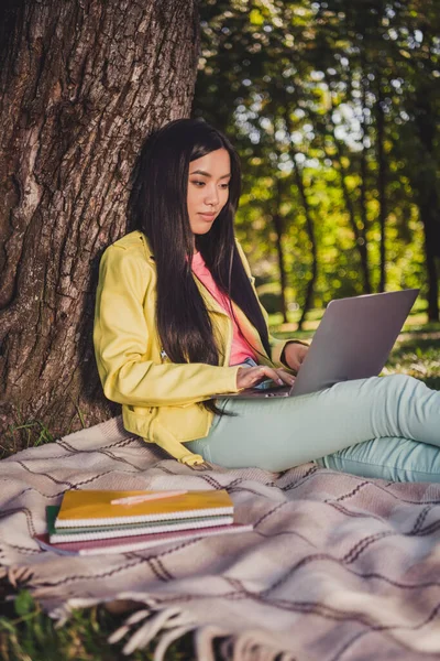 Çekici odaklı neşeli kızın dikey portresi kapakta oturmuş laptopla kompozisyon yazıyor açık havada sohbet ediyor. — Stok fotoğraf