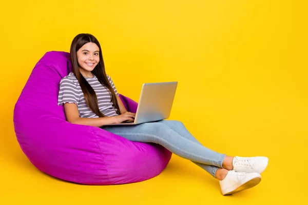 Foto sisi profil tubuh penuh dari wanita muda yang duduk dengan mengenakan beanbag ungu santai menggunakan laptop yang terisolasi dengan latar belakang warna kuning — Stok Foto