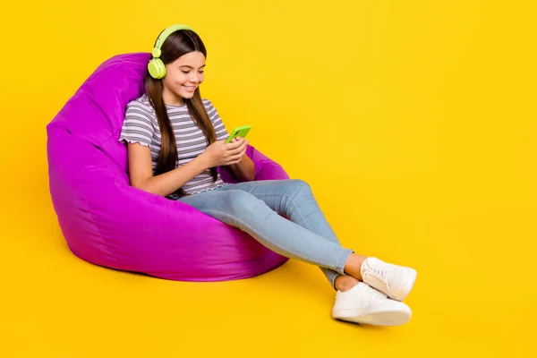 Foto lateral de perfil de tamanho completo de uso de menina jovem móvel como compartilhar sentar violeta beanbag blogger isolado sobre fundo de cor amarela — Fotografia de Stock