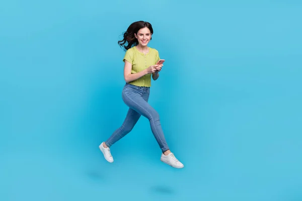 フルサイズ写真のかなり千年のブルネット女性行くタイプ電話着用tシャツジーンズ靴隔離された上青の背景 — ストック写真