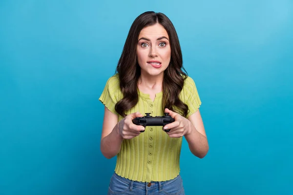Zdjęcie smutna młoda brunetka lady playstation bite usta nosić zielony t-shirt odizolowany na niebieskim tle — Zdjęcie stockowe