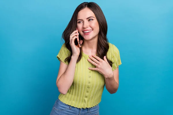 Foto van onder de indruk millennial brunette golvend kapsel dame praten telefoon dragen groen top geïsoleerd op blauwe kleur achtergrond — Stockfoto
